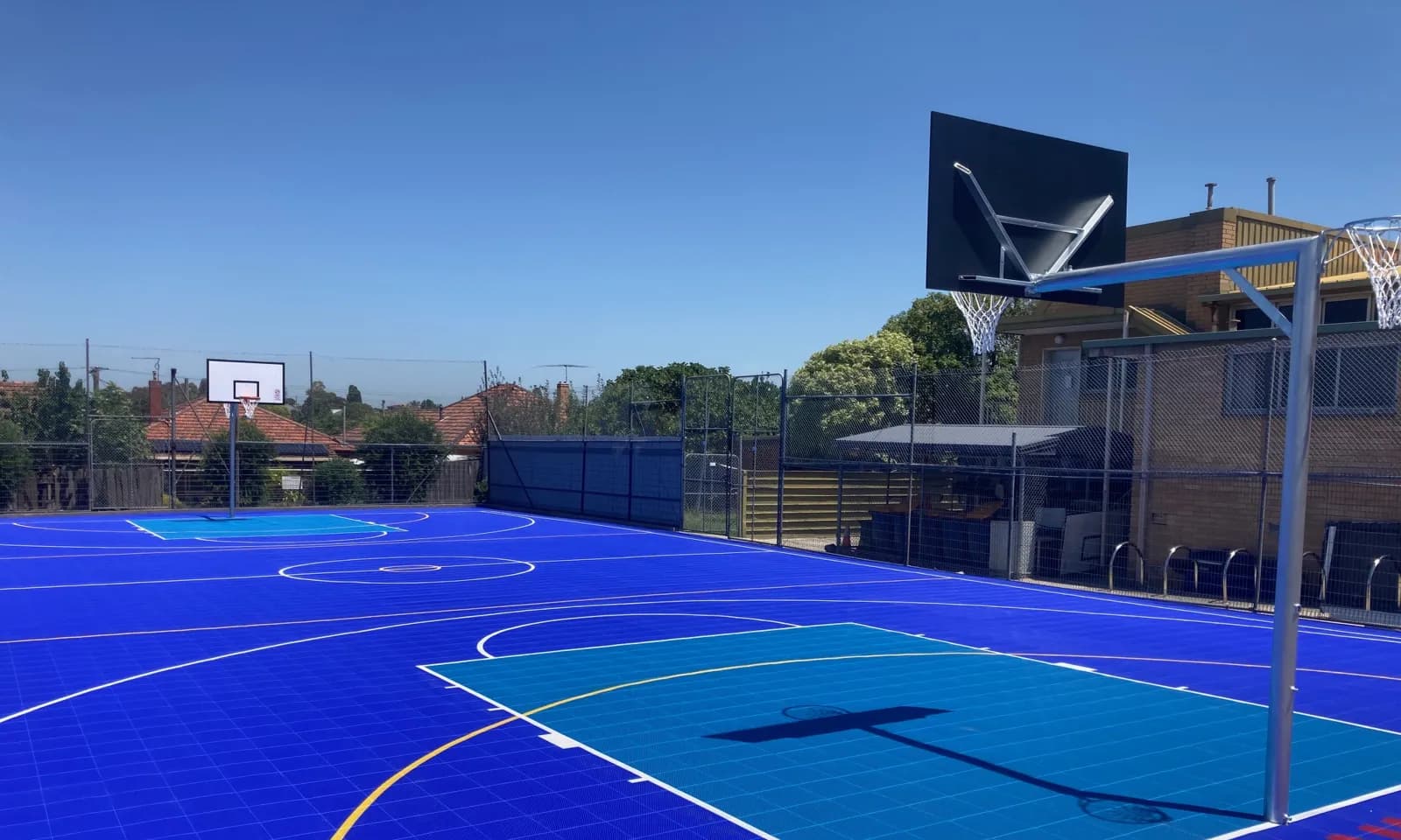 School multi-sport court on blue modular tiles with basketball hoops and coloured court lines